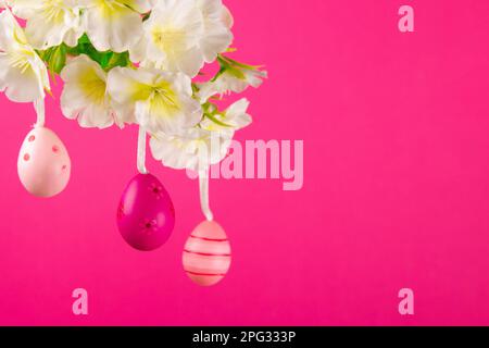 Three pastel pink Easter eggs dangle from a beautifully adorned branch, which stands out against a striking pink background Stock Photo