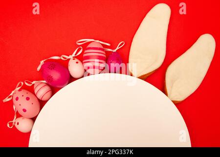 Easter eggs, white circle, and bunny ears decorate a red background Stock Photo