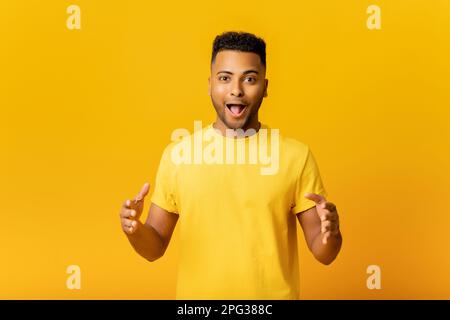 Excited surprised Indian man holding hands in front of him, presenting something, shocked arab guy holding empty space for your product isolated on yellow, demonstrates size. Mockup concept Stock Photo