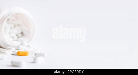 White pills and orange one spilled out of a plastic jar. Medicine capsules on white background. with copy space. Stock Photo