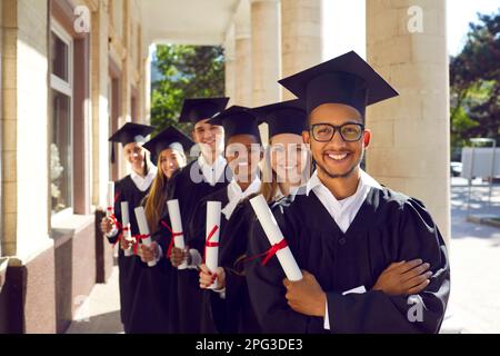 Groups of happy and joyful graduates in academic gowns and academic caps holding scrolls of diplomas Stock Photo