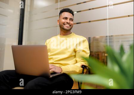 Cheerful determined young bearded male student of freelancer, office worker in casual clothes, sitting in modern coworking space, typing on laptop, man is working on project, writing email to client Stock Photo
