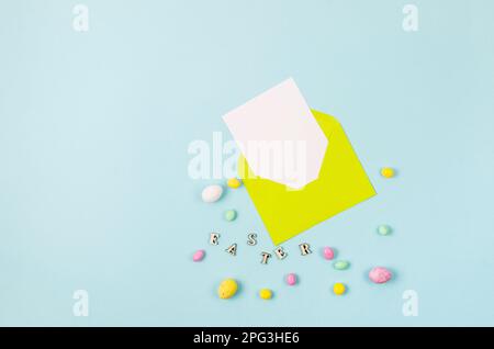 Colorful candy easter eggs on blue background and yellow envelope with blank card with place for text. Easter holiday and tradition concept. Stock Photo