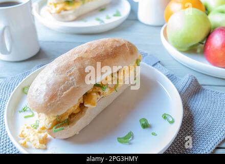 Breakfast sandwich with scrambled eggs and mug of coffee in the morning on a kitchen table at home Stock Photo