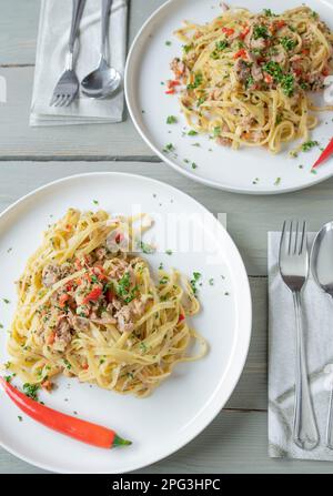 Italian pasta dish aglio e olio. Tagliatelle noodles with olive oil, garlic, parsley and chili peppers. Cooked with tuna and served on plates Stock Photo