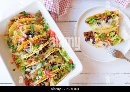 Taco casserole with ground beef, kidney beans, cheese, tomtoes and lettuce in a casserole dish on white background Stock Photo