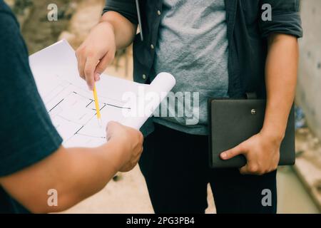 Team of construction workers discussing project details with blueprint in construction site. Stock Photo