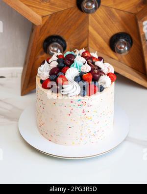 Happy birthday cake with sprinkles, cherries, strawberries, blueberries and meringues Stock Photo