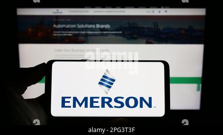 Person holding smartphone with logo of US company Emerson Electric Co. on screen in front of website. Focus on phone display. Stock Photo