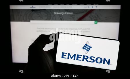 Person holding cellphone with logo of US company Emerson Electric Co. on screen in front of business webpage. Focus on phone display. Stock Photo