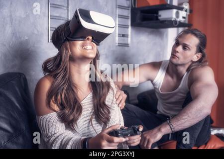 Cheerful modern couple of caucasian guys play together in living room of their studio house. Male guy enjoyng life with a girl playng videogames with Stock Photo