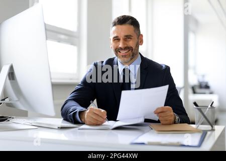 Successful male entrepreneur working with computer and papers at workplace in office, managing financial reports Stock Photo