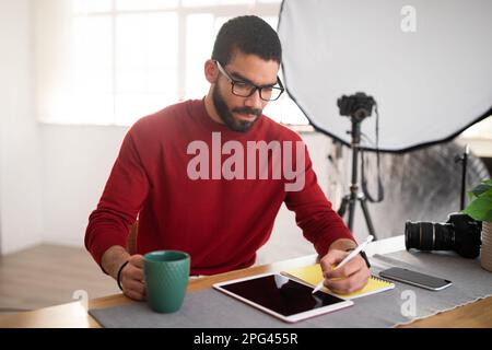 Handsome photographer working on digital pad at office, drinking coffee Stock Photo