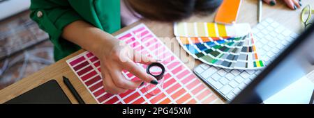 Woman chooses through magnifying glass color and shades on color palette Stock Photo