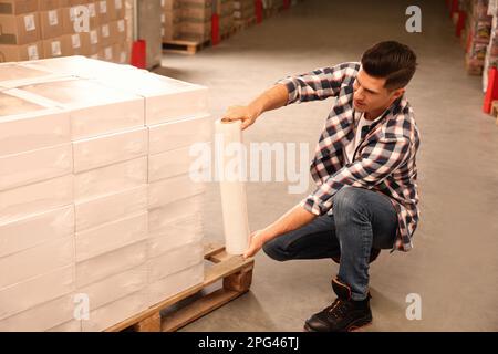 Worker wrapping boxes in stretch film at warehouse Stock Photo