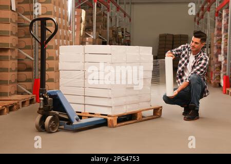 Worker wrapping boxes in stretch film at warehouse Stock Photo