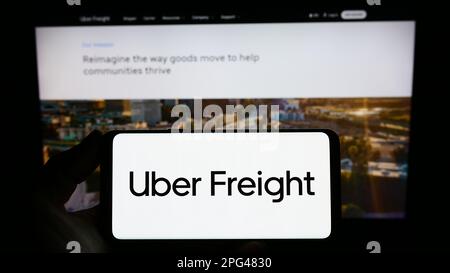 Person holding smartphone with logo of US logistics company Uber Freight on screen in front of website. Focus on phone display. Stock Photo