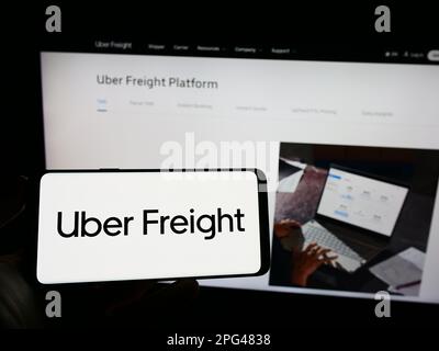 Person holding mobile phone with logo of American logistics company Uber Freight on screen in front of business web page. Focus on phone display. Stock Photo