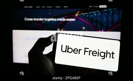 Person holding cellphone with logo of US logistics company Uber Freight on screen in front of business webpage. Focus on phone display. Stock Photo