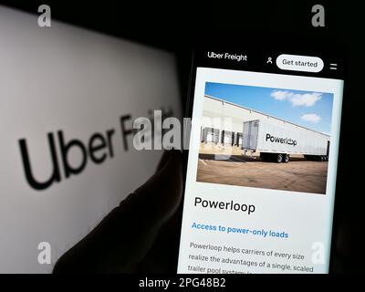 Person holding cellphone with webpage of American logistics company Uber Freight on screen in front of logo. Focus on center of phone display. Stock Photo