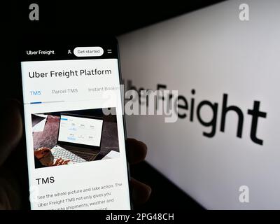 Person holding smartphone with web page of US logistics company Uber Freight on screen in front of logo. Focus on center of phone display. Stock Photo