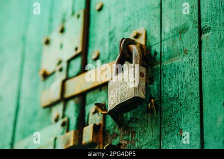 An old vintage metal padlock closes the wooden painted gate with a latch. Closed. Stock Photo