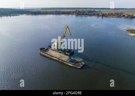 aerial view on crane extracts minerals from bottom onto huge barge in middle of lake or sea Stock Photo