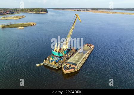 aerial view on crane extracts minerals from bottom onto huge barge in middle of lake or sea Stock Photo