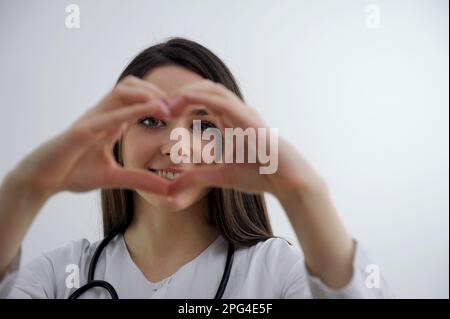 Cute Little Indian girl doctor examining Stuffed heart toy with stethoscope while wearing Doctor's uniform. Standing isolated over white background. High quality photo Stock Photo