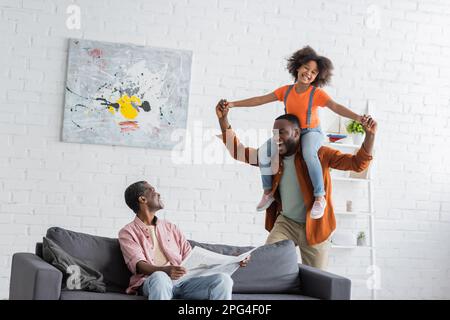 African american grandparent holding newspaper near son and granddaughter having fun at home,stock image Stock Photo