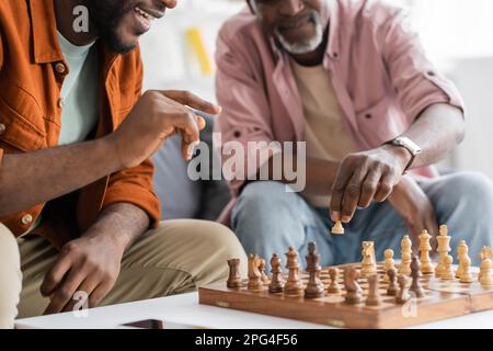 Cropped view of smiling afrcan american man pointing at chess board while playing with dad at home,stock image Stock Photo