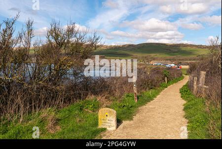 Gravel path leading to Kimmeridge Bay car park with Coastal stone marker showing the distance to Lulworth Cove on the south west coast path Stock Photo
