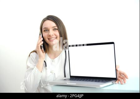woman doctor working on the phone answering the call in front of her laptop with white screen space for advertising A woman doctor consultant with a laptop on a white background. High quality photo Stock Photo