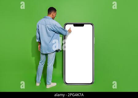 Full body photo of young man using huge phone touchscreen surfing in social media isolated on green color background Stock Photo