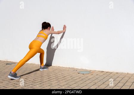 Fit sporty woman doing stretching exercises against a wall. Stock Photo