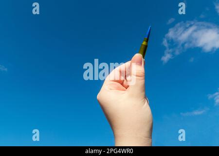 Yellow-blue rifle cartridge in hand against the blue sky (national symbols of Ukraine). The concept of military support for Ukraine Stock Photo