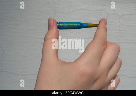 Yellow-blue rifle cartridge with the inscription UKRAINE in hand against a white wall. The concept of military support for Ukraine Stock Photo