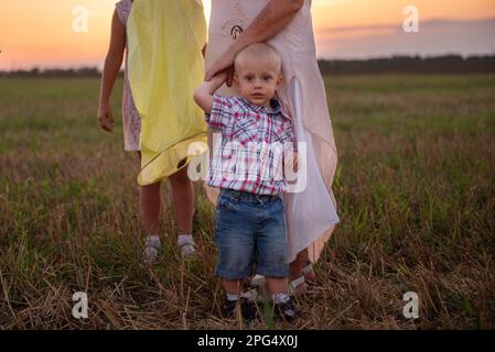Close-up portrait of little boy in plaid shirt, hugging mothers hand. Smiling toddler with blue eyes with sister in the field. The concept of parental Stock Photo
