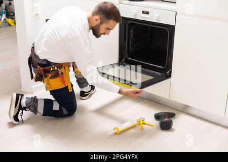 repairman examining oven with screwdriver in kitchen with tool case Stock Photo