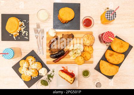 Set of black plates full of typical Colombian paisa food recipes, with roasts, tropical fruit juices, corn empanadas, cheesecake Stock Photo