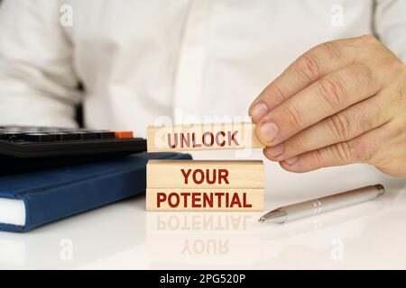 Business concept. In the hands of a businessman, wooden blocks with the inscription - Unlock Your Potential, next to a notebook and a calculator. Stock Photo