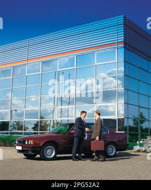 Business executives standing outside modern commercial building with vintage BMW car. Stock Photo