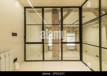 Loft apartment with vintage wooden beams and pillars, exposed brick walls, glass partitions with black metal frames, smooth white concrete floors and Stock Photo