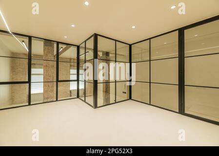 Loft apartment with vintage wooden beams and pillars, exposed brick walls, glass partitions with black metal frames, smooth white concrete floors and Stock Photo