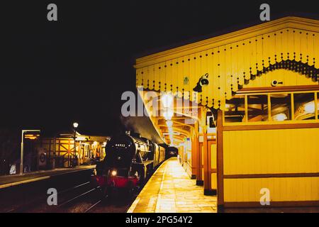A Black 5 steam locomotive, pulling one carriage, going west through Grade 2 listed Hanwell station at night. Downside island platform in foreground. Stock Photo