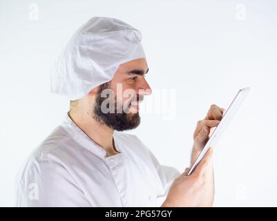 Young male chef using a tablet, reading a recipe. Isolated on a white background Stock Photo