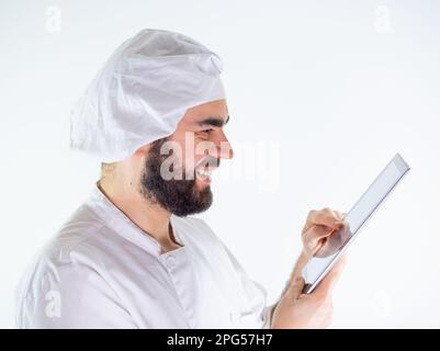 Young male chef using a tablet, reading a recipe. Isolated on a white background Stock Photo