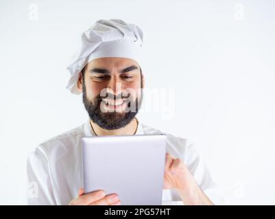 Young male chef using a tablet, reading a recipe. Isolated on a white background Stock Photo