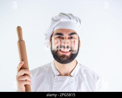 Young male chef showing a wooden rolling pin while smiling and looking at camera. Isolated on a white background Stock Photo