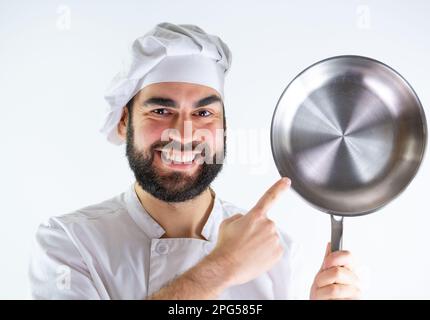 Young male chef showing a stainless pan while smiling and looking at camera. Isolated on a white background Stock Photo